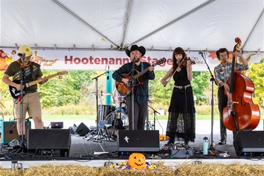 A band performs on the Hootenanny Stage at the City of Des Plaines annual Harvest Hoot, featuring two guitarists, a violinist, and an upright bass player.