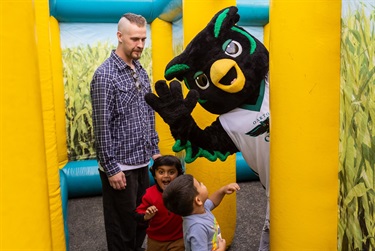 Two young boys and an older man pose with Oakley, the Oakton College owl mascot, inside an inflatable corn maze at the City of Des Plaines annual Harvest Hoot.