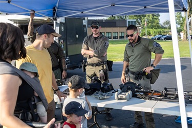 Des Plaines police officers display tactical gear behind a table while people watch.