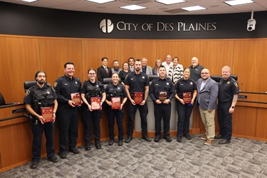 A group of Des Plaines police officers stand with plaques in City Hall chambers after receiving Life Saving Awards.