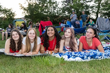 A group of young girls smiling while lying on a picnic blanket on the lawn.