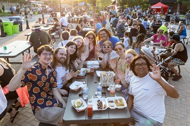 Young people smiling for a photo while seated with food at the Food Truck Round Up.
