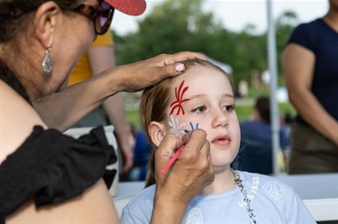 A girl getting her face painted with a fireworks design.