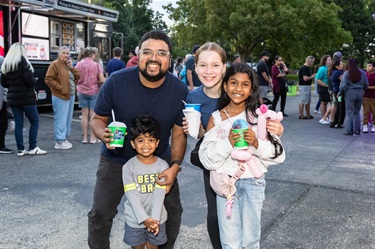 Two adults and two children holding up food and smiling with a food truck in the background at the Food Truck Round Up.